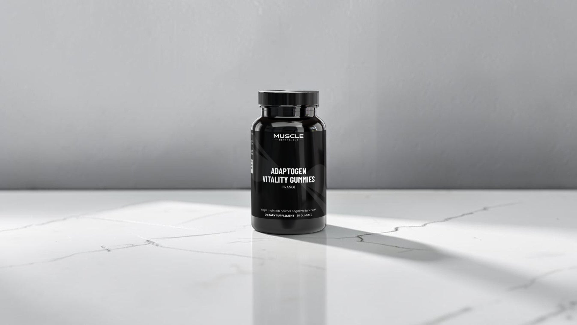 A black bottle of Muscle Department Adaptogen Vitality Gummies stands on a white marble surface against a gray wall, with soft sunlight casting a shadow.