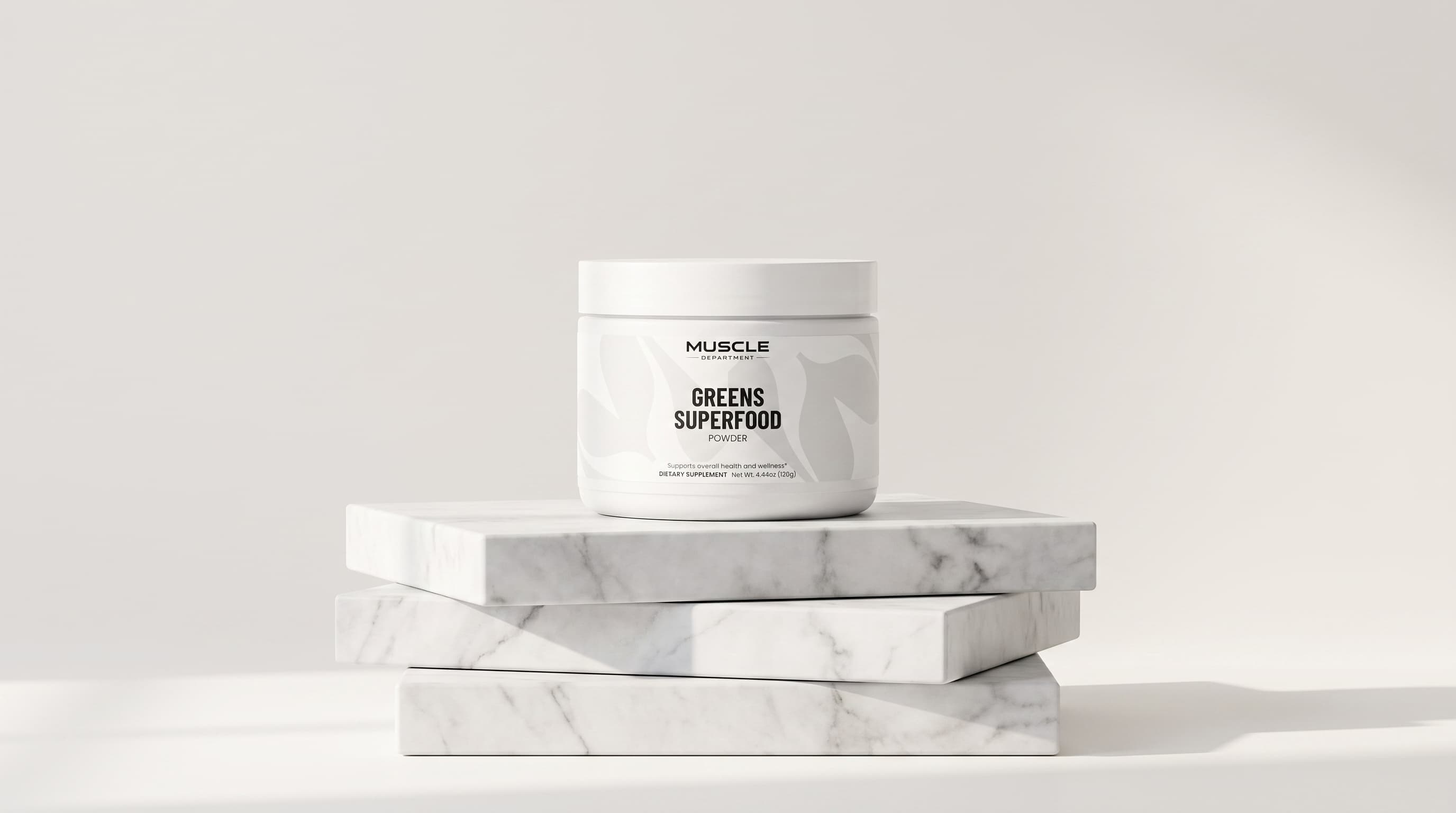 A white plastic jar of Muscle Department Greens Superfood powder sits on top of three stacked white marble display blocks against a clean, light gray studio background.